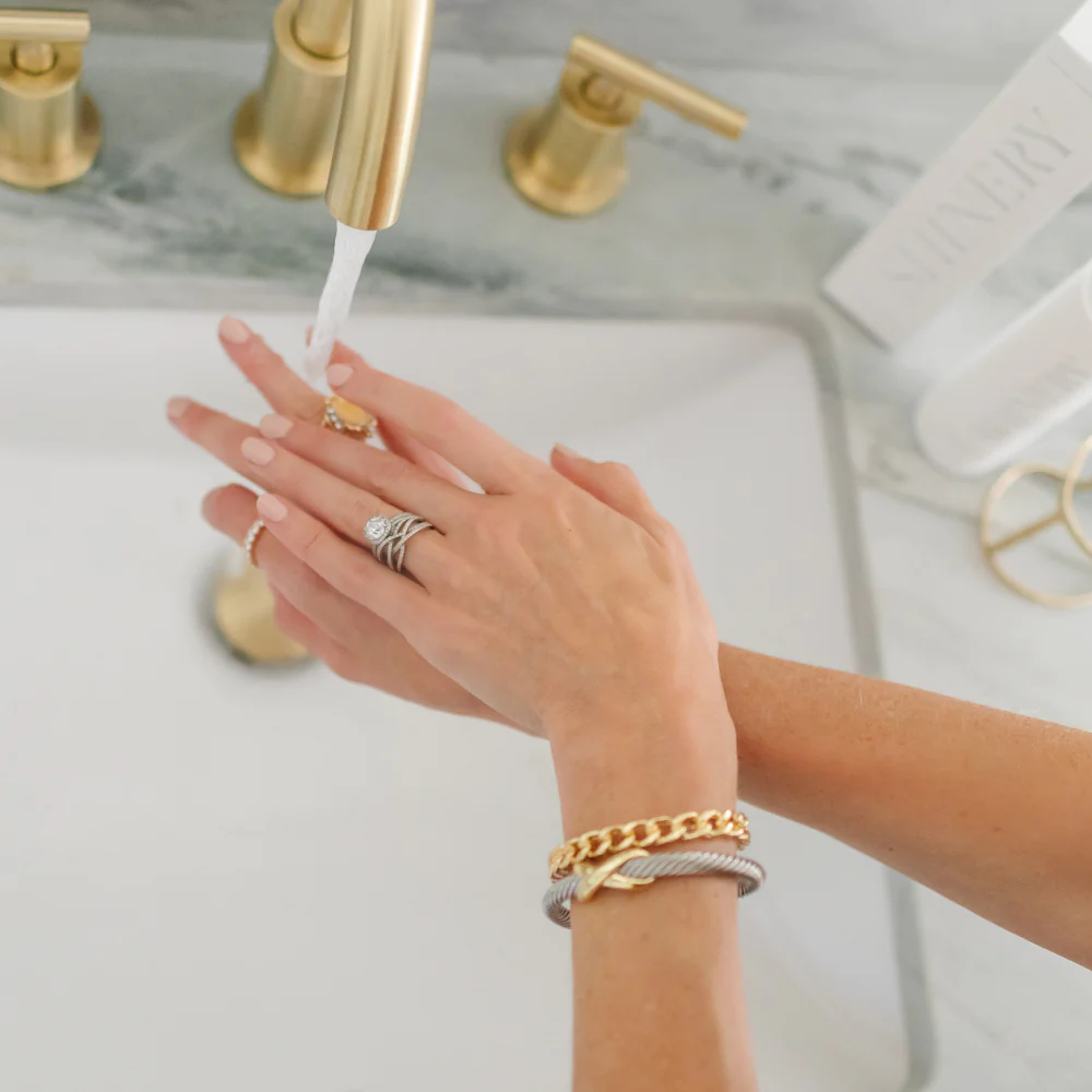 Hands wearing rings and bracelets being washed at a sink with Shinery jewelry wash.