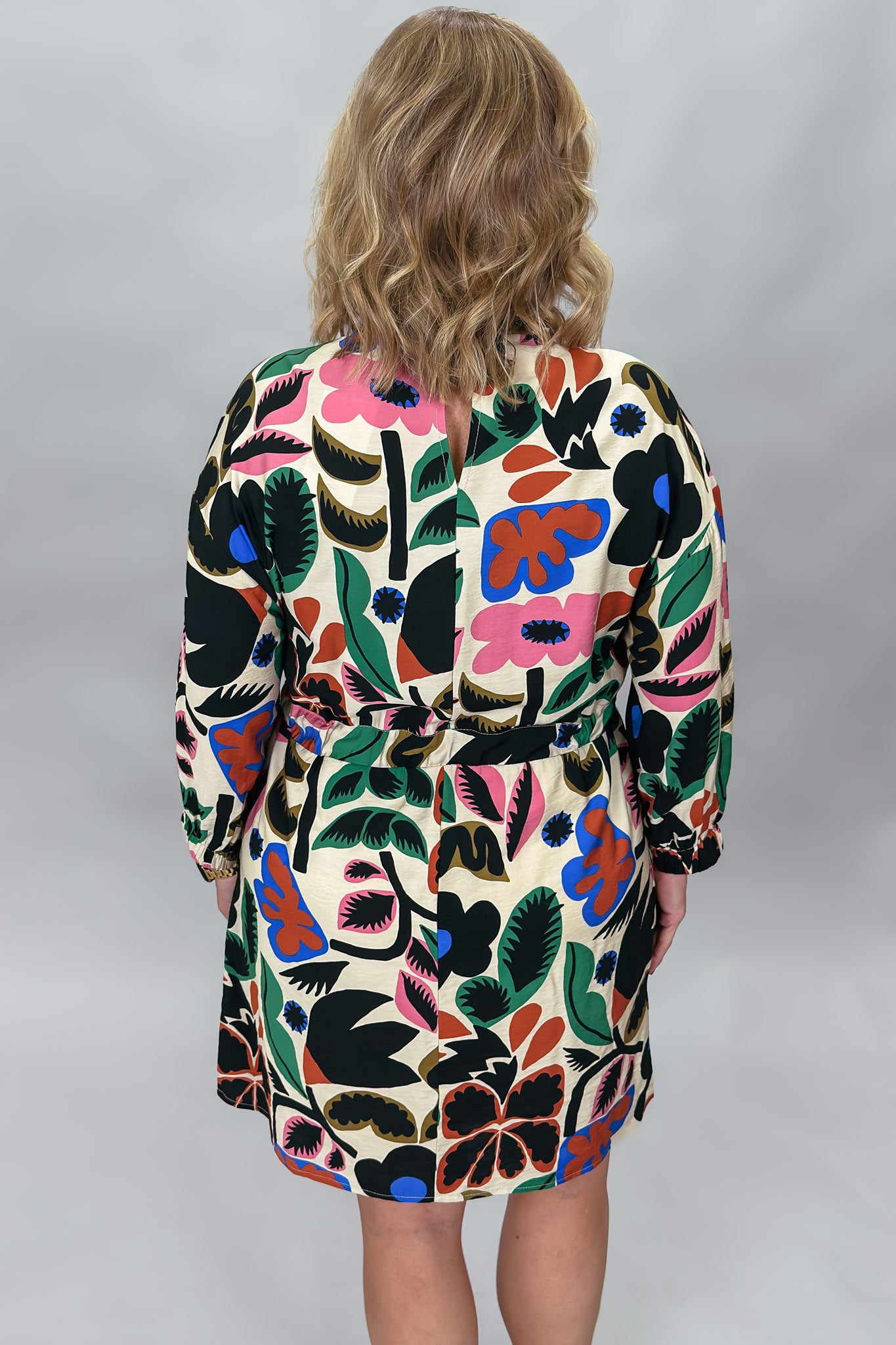 Back view of the Back On 74 bold floral print midi dress on a model, showing the belted wrap waist, long sleeves, knee-length hem, and multicolor botanical print on cream.