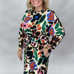 Front studio portrait of a model in the Back On 74 bold floral print midi dress, highlighting the colorful oversized flowers and leaves across the cream fabric, long sleeves, and relaxed waist.
