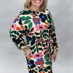 Model in the Back On 74 bold floral print midi dress, posed with one hip angled in a studio to show the flowing midi skirt, long sleeves, and colorful botanical print on cream.