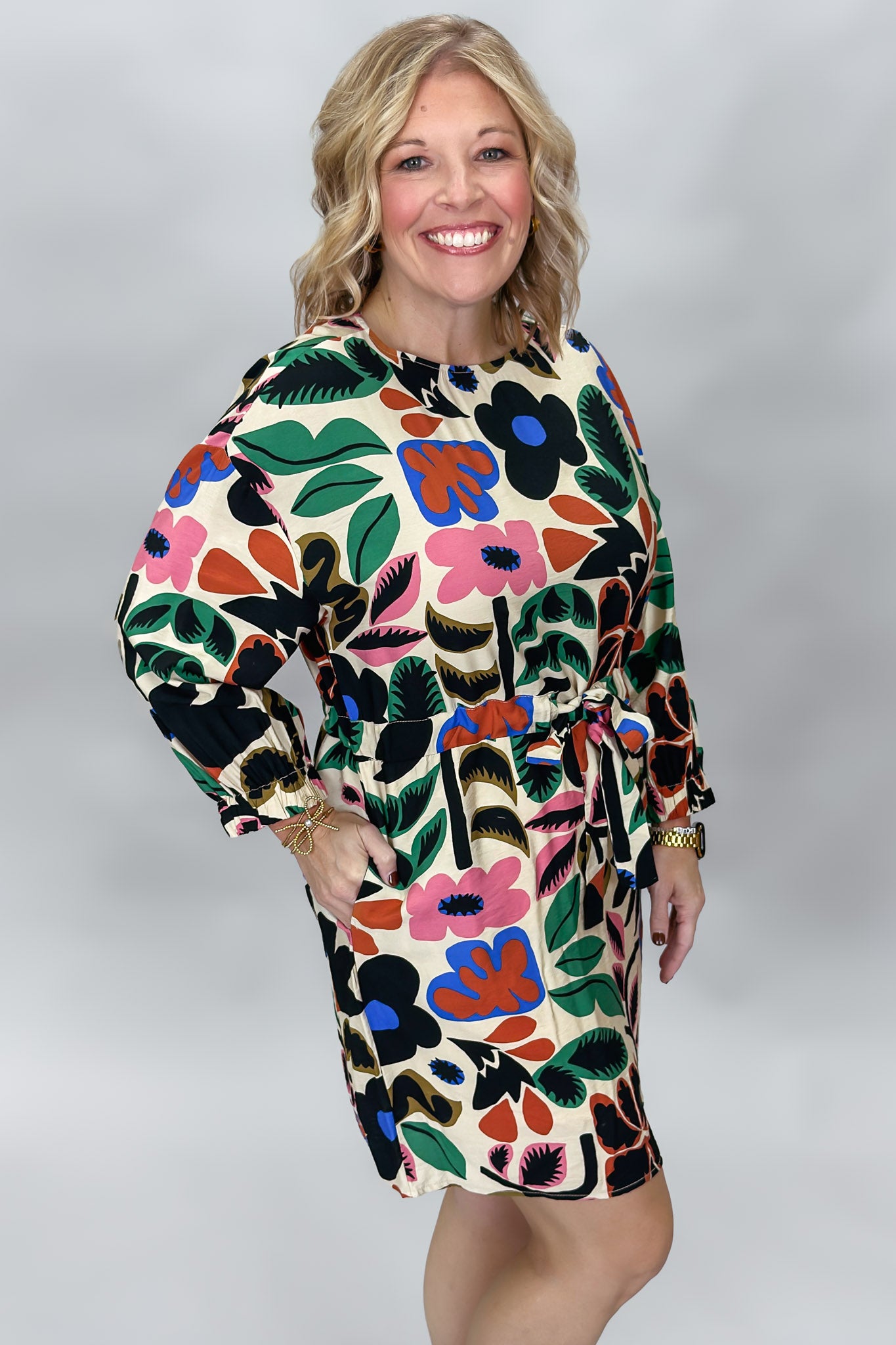 Model in the Back On 74 bold floral print midi dress, posed with one hip angled in a studio to show the flowing midi skirt, long sleeves, and colorful botanical print on cream.