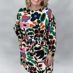 Three-quarter front view of the Back On 74 bold floral print midi dress on a model, highlighting its belted silhouette, long sleeves, knee-length cut, and large colorful floral print against cream.
