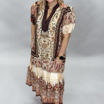 Blown My Cover cream bohemian floral midi dress in a full-length three-quarter pose, showing puff sleeves, a dark tie neckline, tiered skirt, and rust paisley print.