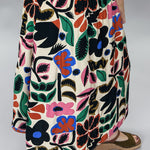 Detail crop of the Candle Flame skirt’s oversized navy, blue, pink, rust, and green floral motifs on a cream background, with the high waist and A-line midi drape visible.