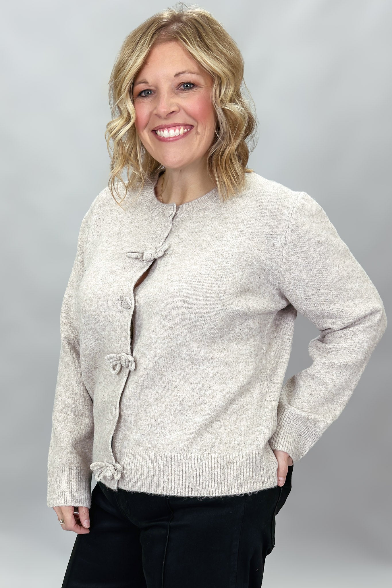 Compania Fantastica tan button-front cardigan with bow details; angled model view.