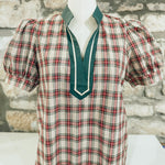 Plaid blouse with green collar on a mannequin against a stone wall background