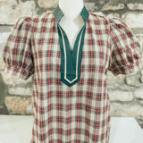 Plaid blouse with green collar on a mannequin against a stone wall background