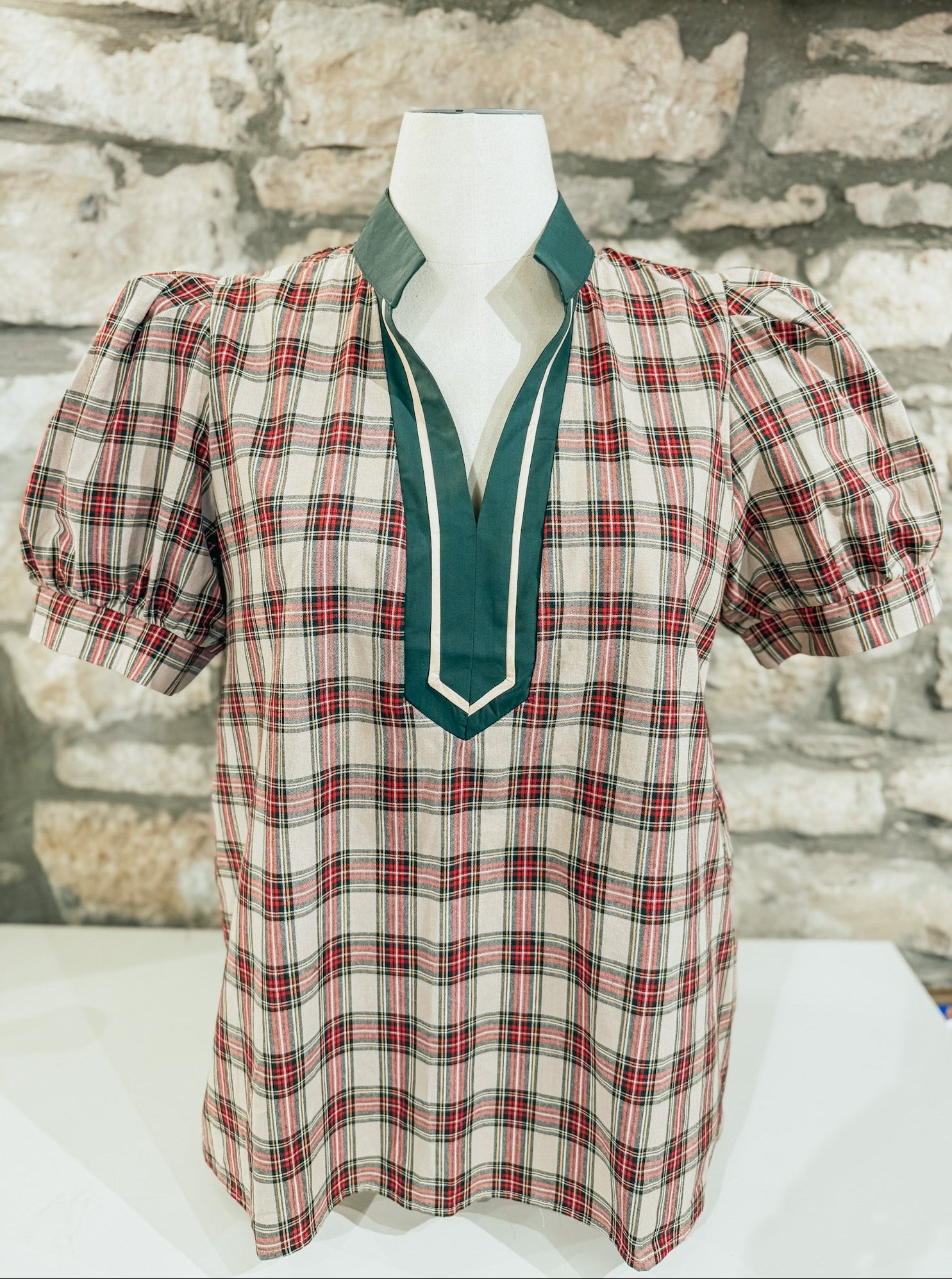 Plaid blouse with green collar on a mannequin against a stone wall background