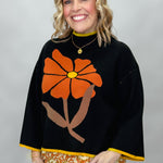 Ivy Jane black mock-neck sweater with a large orange flower; angled model view.