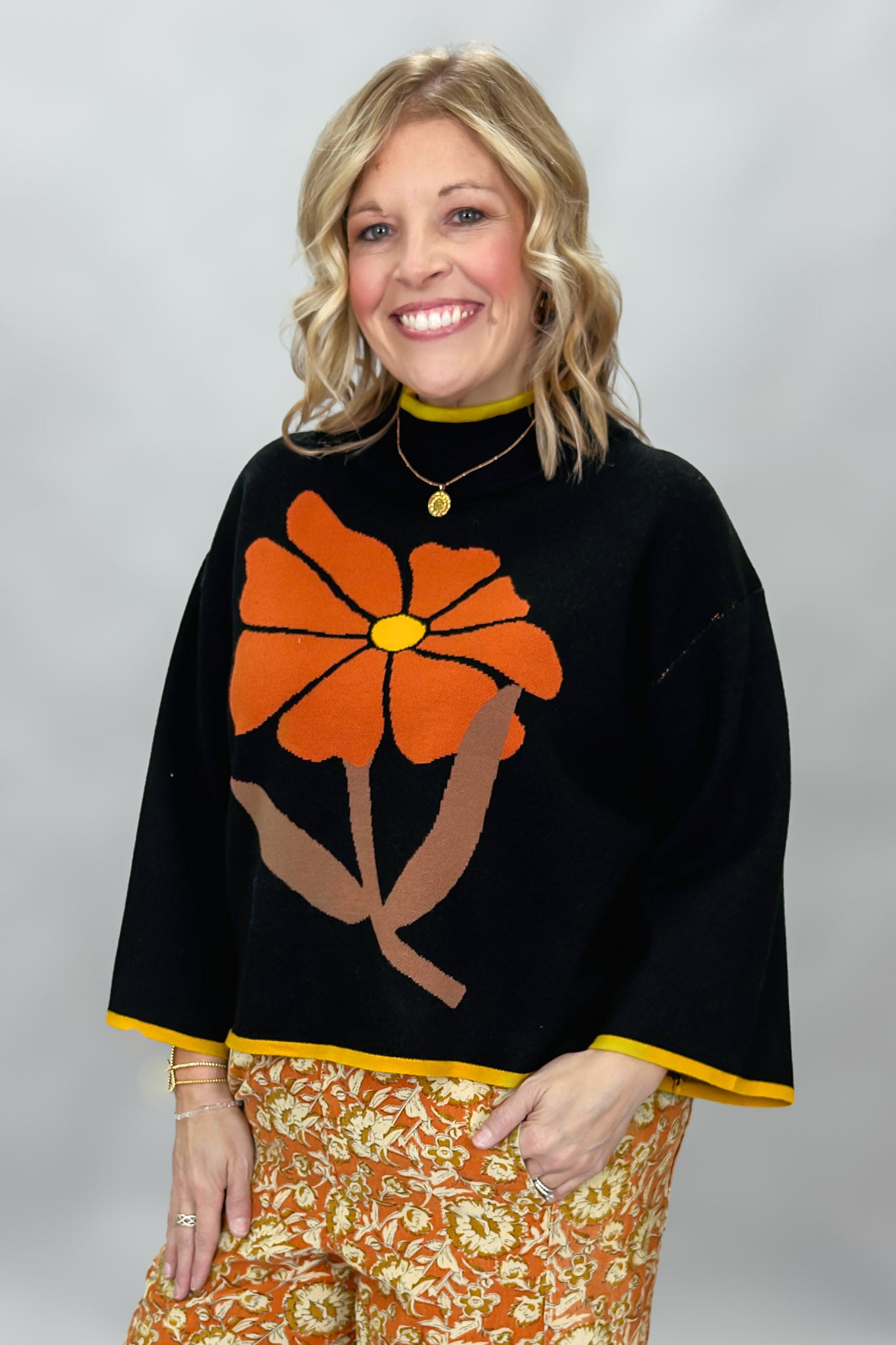 Ivy Jane black mock-neck sweater with a large orange flower; angled model view.
