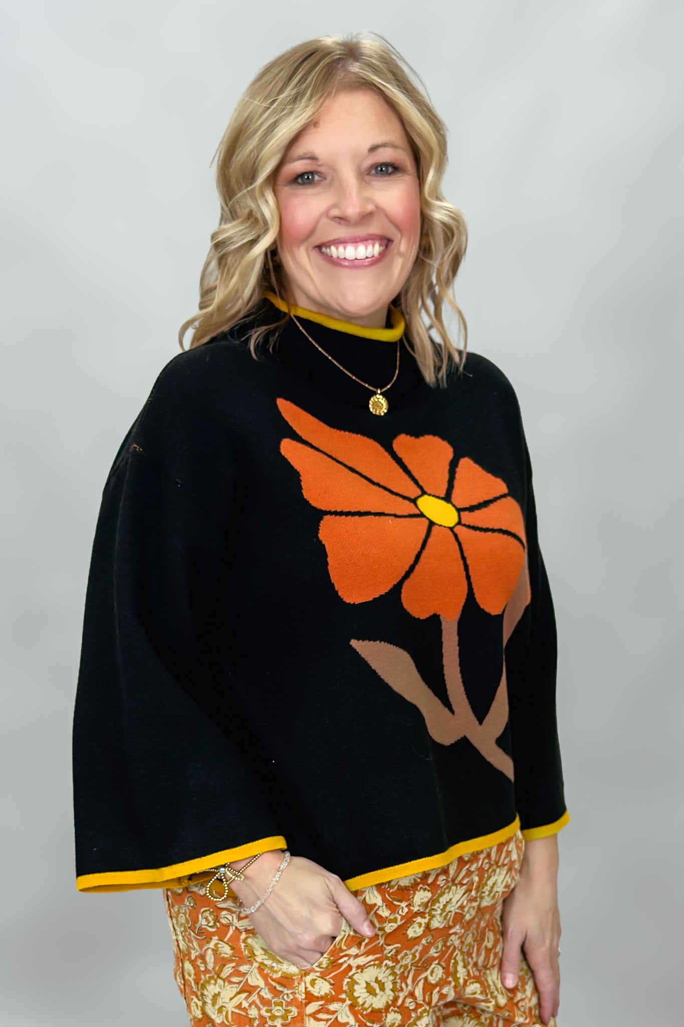 Ivy Jane black mock-neck sweater with a large orange flower; angled model view.