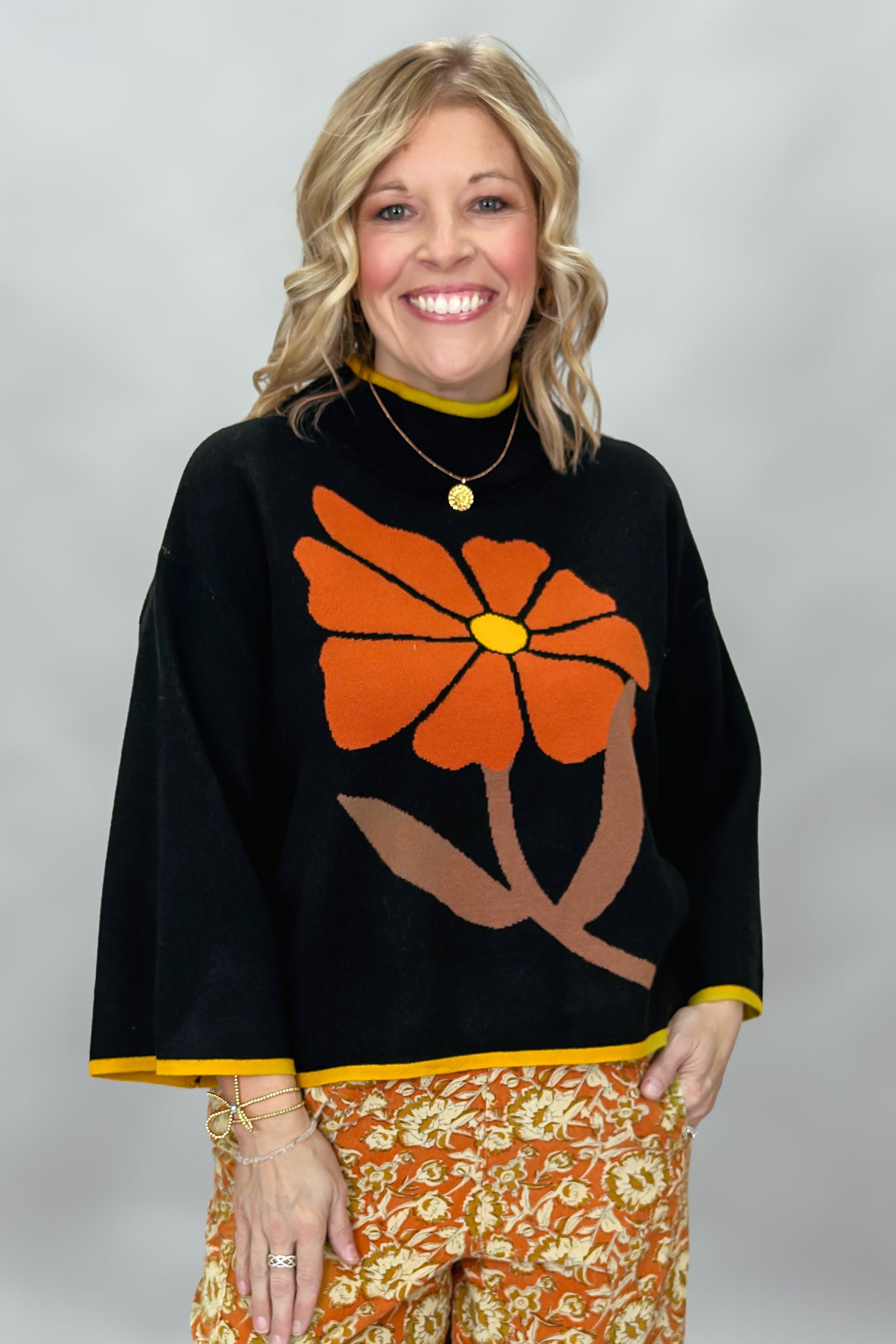 Ivy Jane black mock-neck sweater with a large orange flower; front model view.