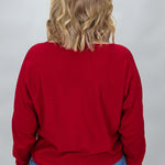 Back view of the Phone, Keys, Wallet red bat-wing sleeve sweater, showing its relaxed shoulder line, full sleeves, ribbed cuffs, and straight hem above blue jeans.