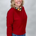 Phone, Keys, Wallet red relaxed knit top in a three-quarter model pose, showing the bat-wing sleeves, roomy body, hip-length hem, and casual fit over blue jeans.