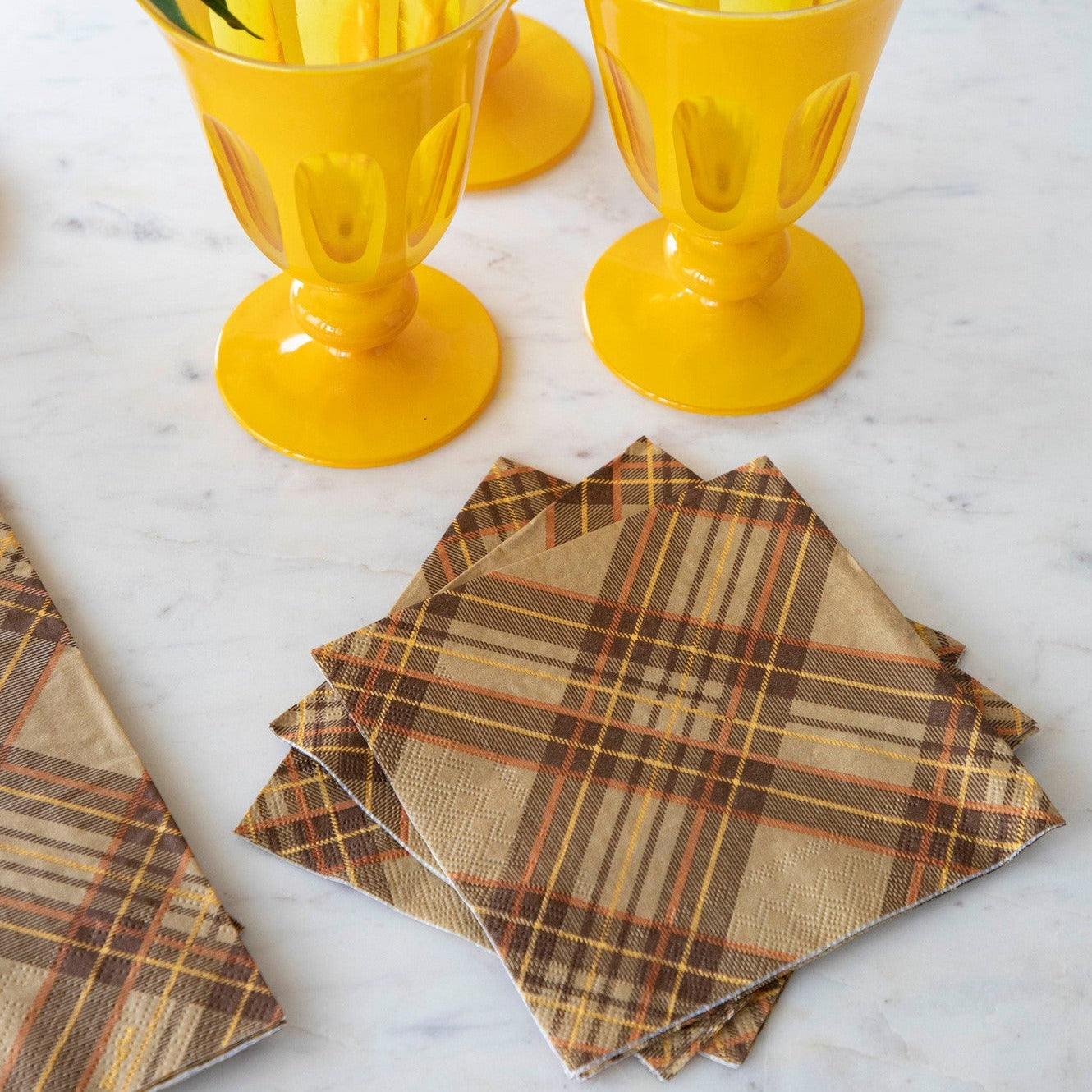 Autumn plaid cocktail napkins arranged with yellow drinking glasses as a serving suggestion